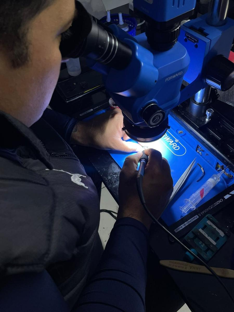 Técnico de CMT reparando una placa con microscopio y cautín